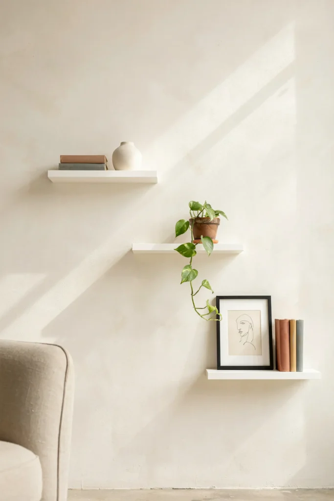 three white floating shelves staggered on a soft cream wall