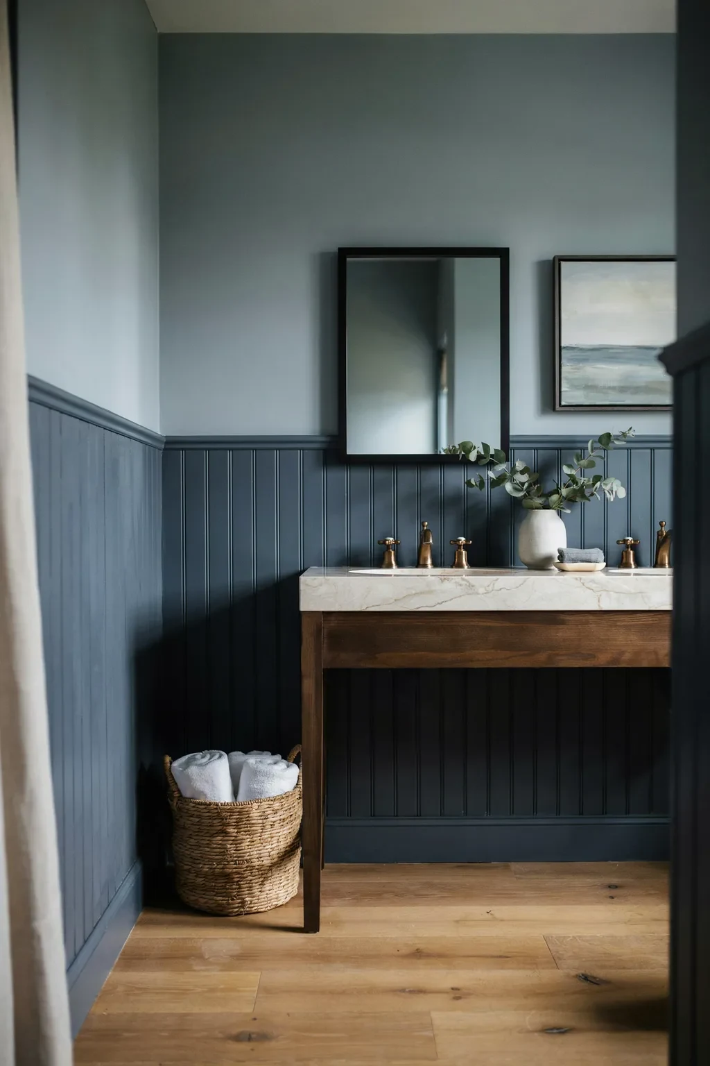 Navy beadboard bathroom with a wood vanity and a seascape painting