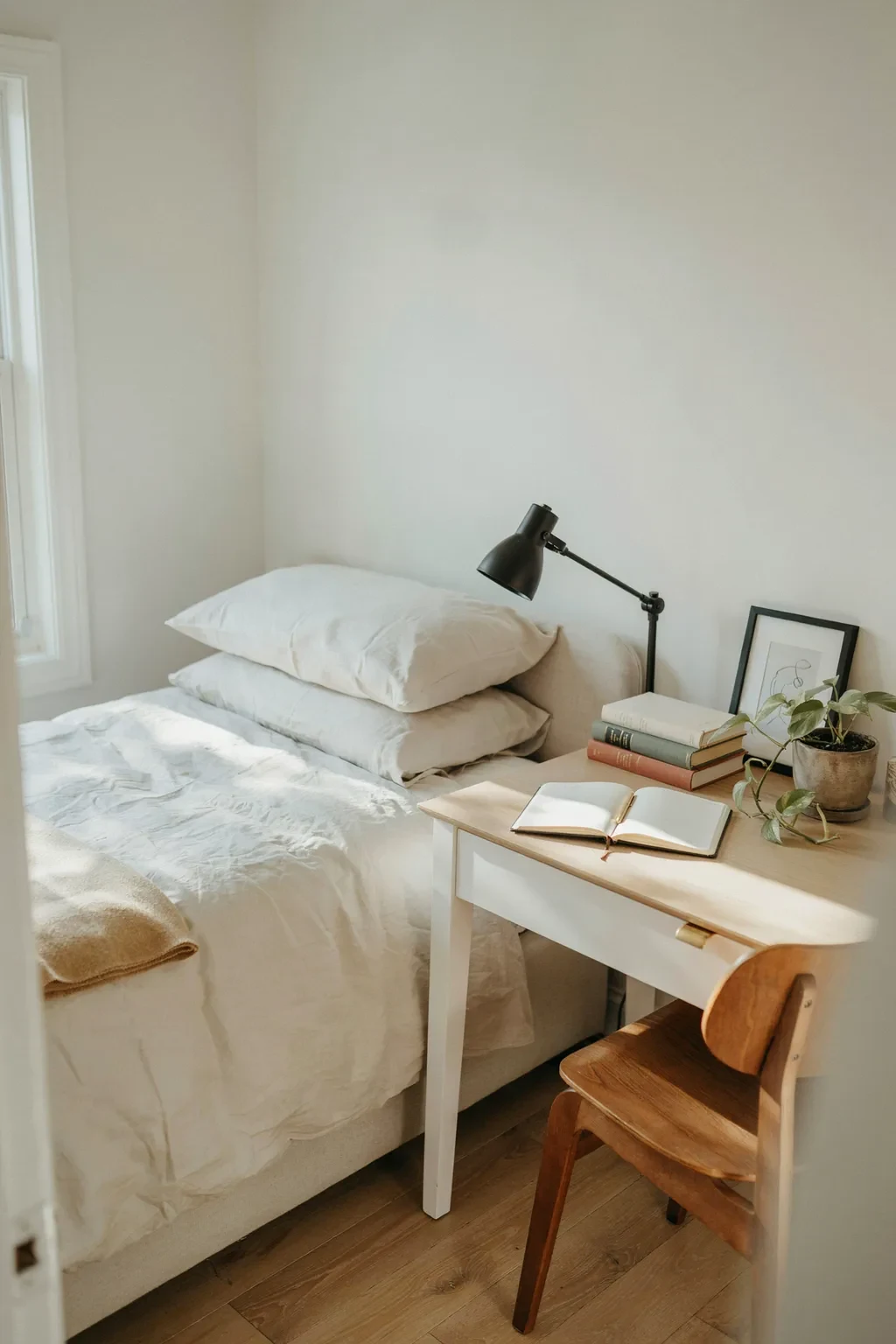 Slim desk beside a bed doubling as a nightstand in a small bedroom