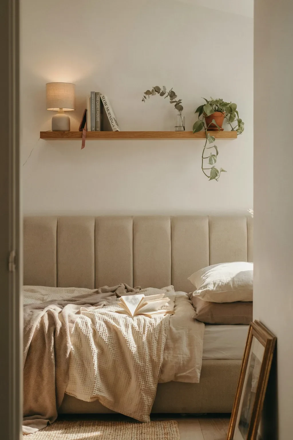 Floating oak wall shelf styled as a bedside nightstand in a small bedroom